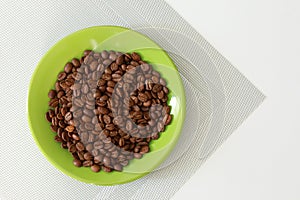 Green saucer with coffee beans on white table