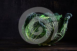 Green savoy cabbage, a healthy winter vegetable in dramatic light on dark and moody rustic wood with copy space