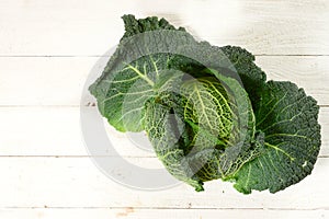 Green savoy cabbage, a healthy winter vegetable, whole head on rustic white wood with copy space, high angle view from above