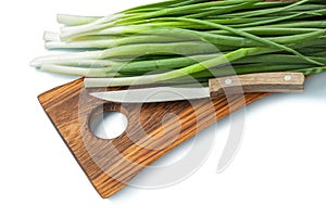 Green scallions stems and kitchen knife on wooden chopping board isolated