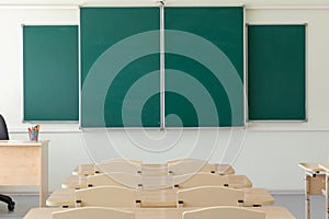 Green school board in the classroom with no pupils. in the foreground are desks and chairs. close-up