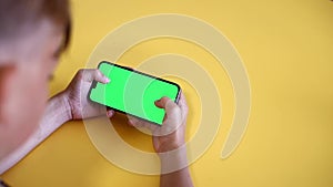 green screen. The child is holding a Smartphone in hand Close-up playing a game. phone with blank green screen mock up