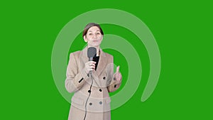 GREEN SCREEN CHROMA KEY Caucasian female TV news reporter in coat holding microphone talking against green background.