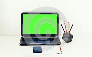 Green screen laptop, smartphone, notebook and pencils in concrete holder on white table, education office concept background