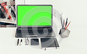 Green screen laptop, smartphone, notebook and pencils in concrete holder on white table, education office concept background