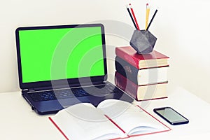 Green screen laptop, smartphone, notebook and pencils in concrete holder on white table, education office concept background