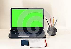 Green screen laptop, smartphone, notebook and pencils on white table, education office concept background