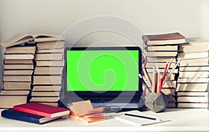 Green screen laptop, stack of books, notebooks and pencils on white table, education office concept background