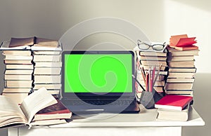 Green screen laptop, stack of books, notebooks and pencils on white table, education office concept background