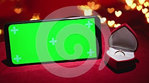 Green screen smartphone with chroma key for Valentine's day. Red background defocused lights hearts