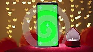 Green screen smartphone with chroma key for Valentine's day. Red background defocused lights hearts