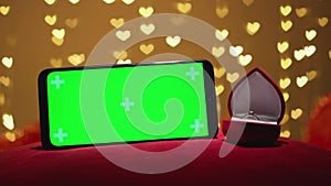 Green screen smartphone with chroma key for Valentine's day. Red background defocused lights hearts