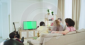 Green screen on tv big group of friends on the sofa in a large spacious living room watching something on tv , multi