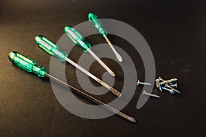 Green screwdrivers and screws on dark grey background