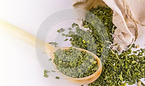 Green seasoning for cooking in a wooden spoon and a bag on sunlight