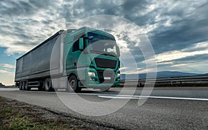 Green semi trailer truck on a highway at sunset