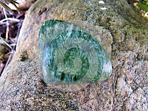 Green seraphinite crystal stone cabochon with angel wings pattern on a rock