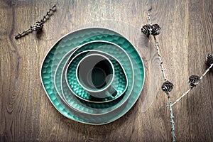 Green set of dishes: a mug, saucer, plates, bowl and dry larch cones on twigs on wooden background. Christmas table decoration,