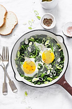 Green shakshuka. Fried eggs with fresh spinach, ramson, leek in a cast iron skillet on a white background