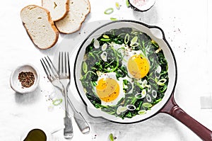 Green shakshuka. Fried eggs with fresh spinach, ramson, leek in a cast iron skillet on a white background