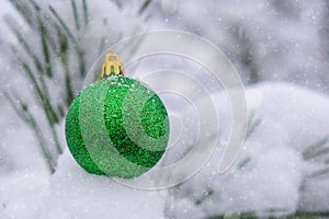 Green shiny trendy Christmas ball on snowy branch firs in winter forest. Winter holiday background. Copy space. Happy