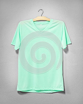Green shirt hanging on cement wall. Empty clothing for design. Front view