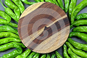 Green Shishito peppers in a circle with a wooden board in the center