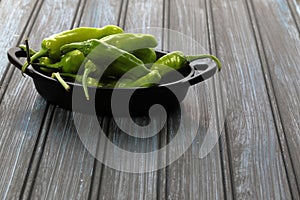 Green Shishito peppers in a metal container on wooden background