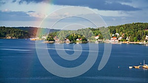 Green shore of Baltic Sea with village and rainbow