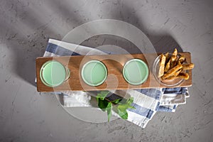 Green Shot cocktail with dried fig on wooden board on grey stone table