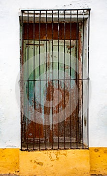 Green shuttered window with black iron bars on white and yellow