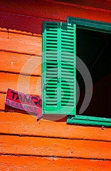 Green shuttered window with orange walls is backdrop for Tango lesson sign in La Boca