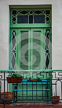 Green shuttered window on white wall with planters and green ban