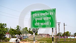 Green sign board with attractive white written language along side road. White written language with green background