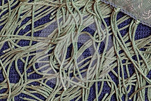 A green silk shawl with a fringe along the edge of the fabric against a dark blue woolen fabric. Abstract background