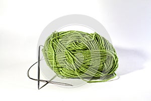 Green skein of wool knitting thread with metal knitting needles for knitting on a white insulated background