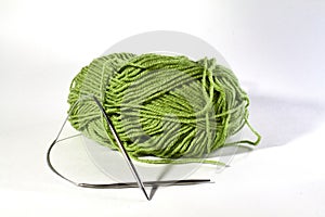 Green skein of wool knitting thread with metal knitting needles for knitting on a white insulated background
