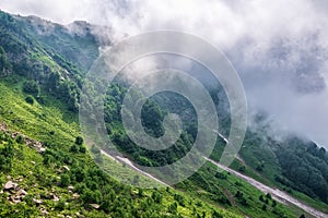 The green slopes of high mountains are hidden in clouds and fog. Melting snow in high mountains in summer