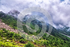 The green slopes of high mountains are hidden in clouds and fog. Melting snow in high mountains in summer