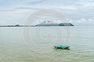 Green small fishng boat parked at the shore of Prachuap Bay with fog on Khao Ta Mong Lai Forest Park background, Thailand