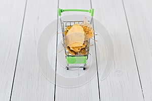 Green small toy shopping cart with yellow birch leaves on a retro wood boards. Autumn Concept.