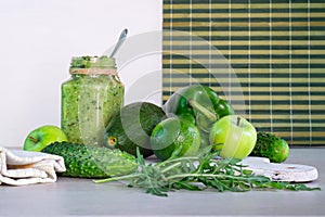 Green smoothie of apple, cucumber, avocado and pepper, whole ingredients on a white and striped background