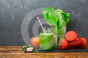 Green smoothie with apple, lettuce and dumbbells over dark background. Detox, dieting, vegetarian, fitness or healthy eating