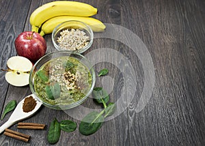 Green smoothie with apples, spinach, banana, germinated buckwheat and cinnamon on a dark wooden background
