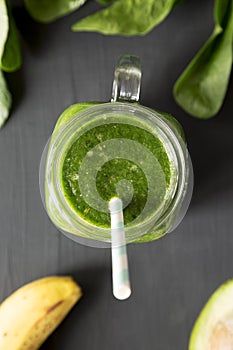 Green smoothie with avocado, spinach and banana in a glass jar over black surface, view from above. Flat lay, top view, overhead