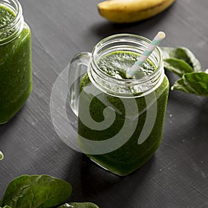 Green smoothie with avocado, spinach and banana in glass jars over black background, side view. Close-up