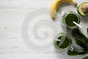 Green smoothie with avocado, spinach and banana in glass jars over white wooden background, top view. Flat lay, overhead, from