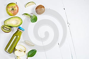Green smoothie in bottl with avocado, apple and kiwi on white wooden background.