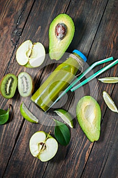 Green smoothie in bottl with avocado, apple and kiwi on white wooden background