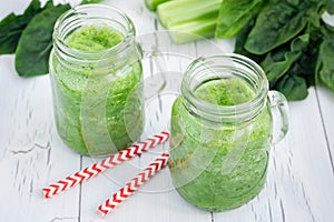Green smoothie with celery, cucumber, spinach, apple and lemon on a white wooden background